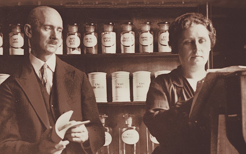 Man and woman standing in front of shelves of jars of various chemical compounds