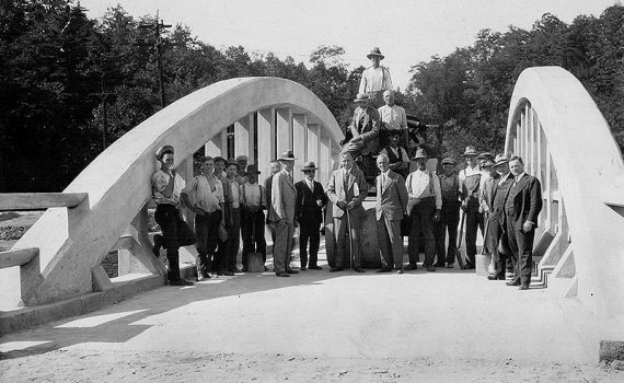 Group of about 21 men, council members and workers, standing on bridge.